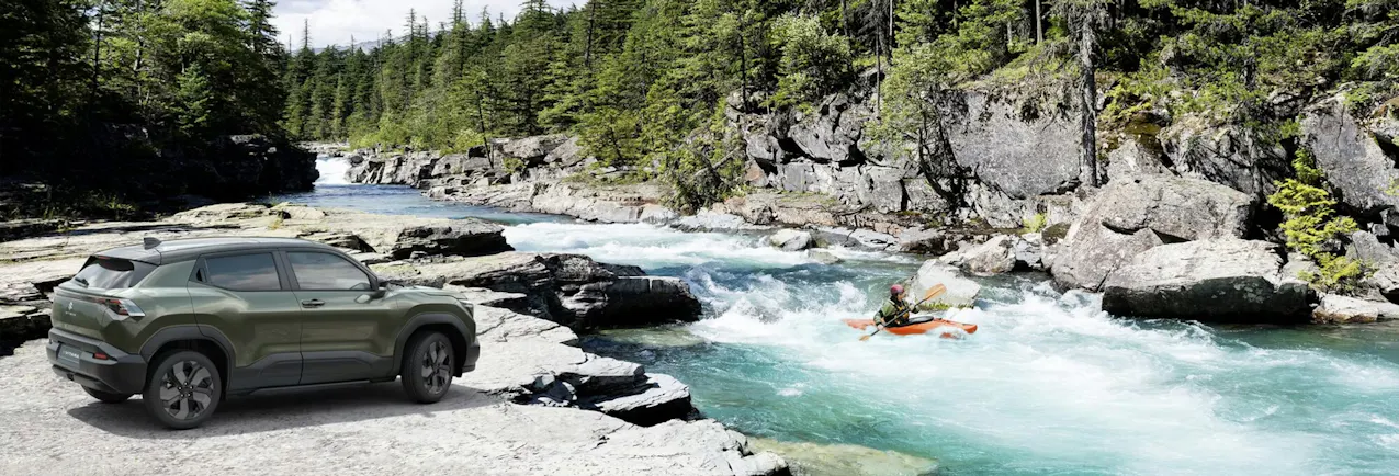 Suzuki E-Vitara in un elegante colore verde, vicino a un torrente di montagna