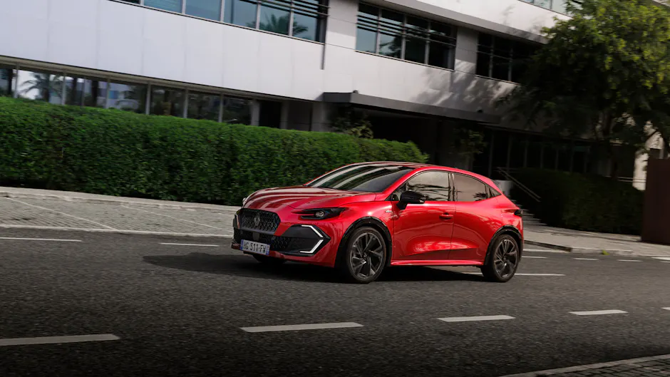 Roter Renault Clio Hybrid in Frontdreiviertelansicht auf urbaner Strasse vor modernem Bürogebäude, sportliches Design.
