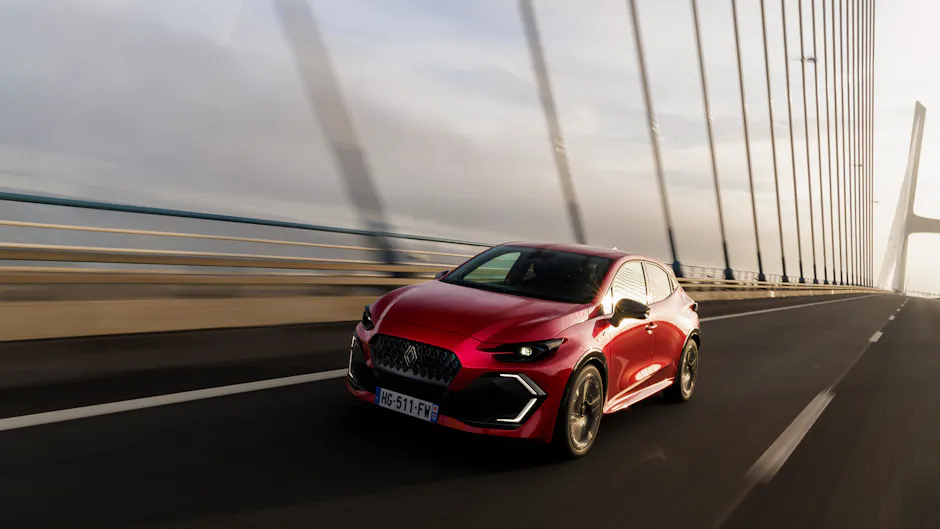 Roter Renault Clio fährt dynamisch über moderne Brücke bei Tageslicht, sportliche Frontansicht.