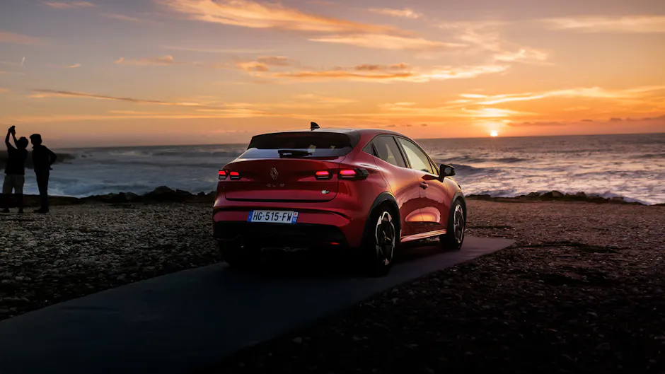 Roter Renault Clio in Heckansicht am Meer bei Sonnenuntergang, modernes Heckdesign und LED-Rückleuchten.