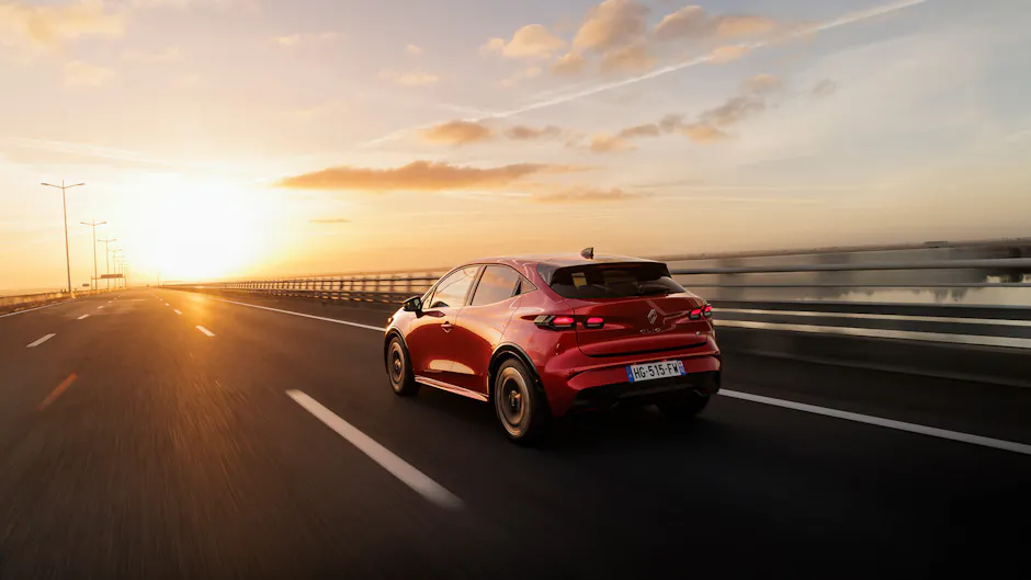 Roter Renault Clio in Heckansicht auf Autobahn bei Sonnenaufgang.