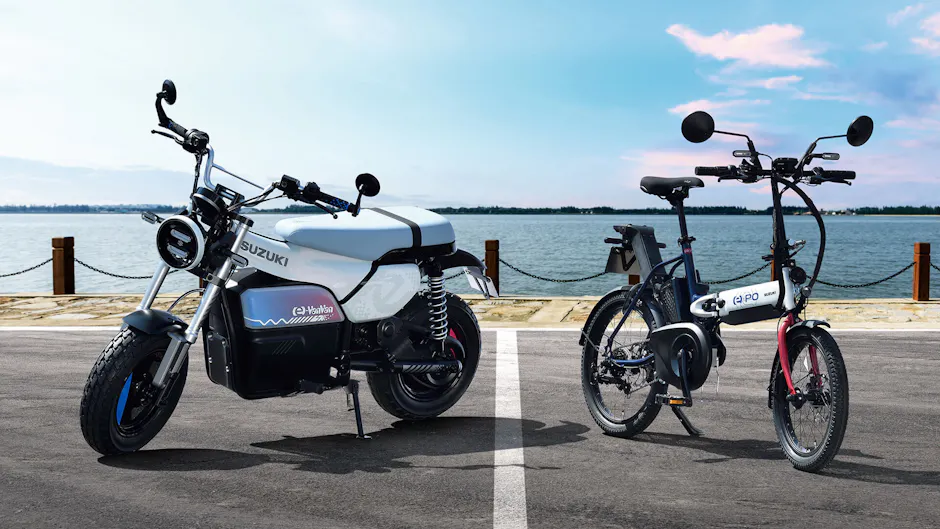 Due veicoli elettrici Suzuki affiancati vicino all’acqua.
