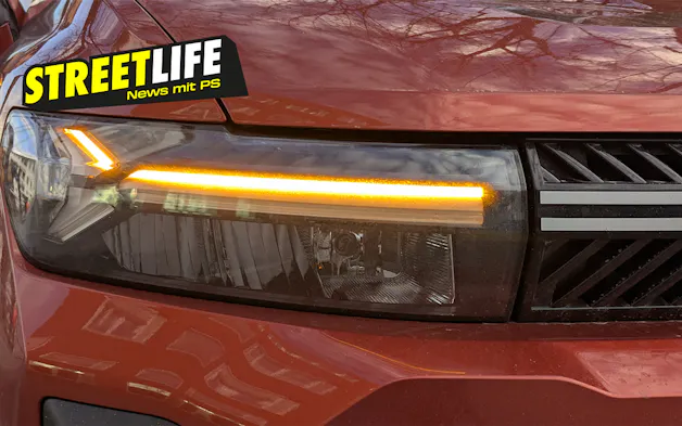 Primo piano di un'auto rossa dotata di moderni fari anteriori a LED, luci diurne luminose e indicatori di direzione accesi nella parte anteriore del veicolo.