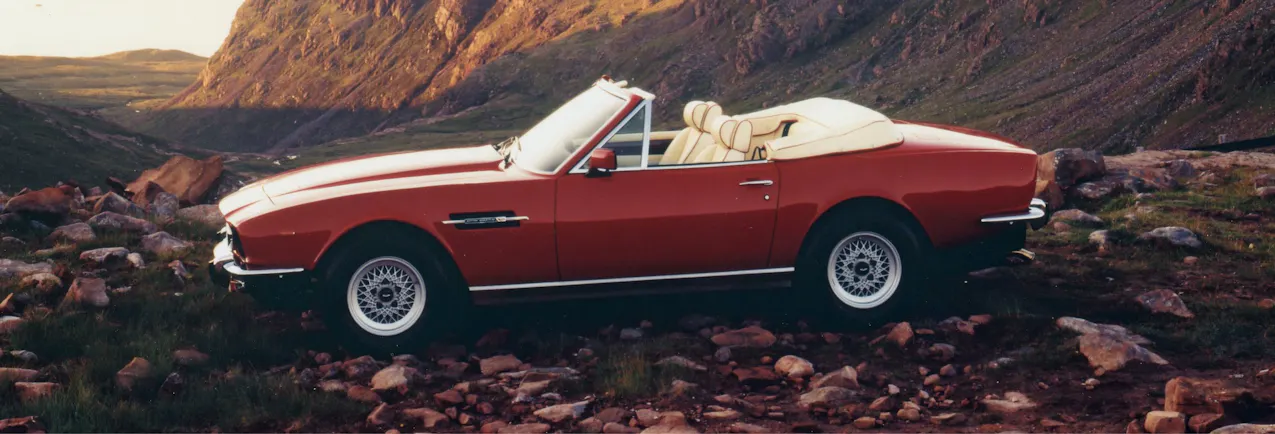 Une vieille Aston Martin rouge décapotable, avec une montagne en arrière-plan