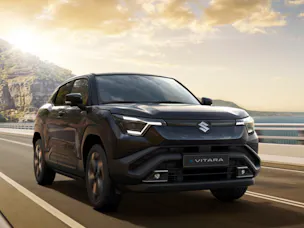 Suzuki E-Vitara in Schwarz, fährt an einer Küste entlang, im HIntergrund ein Sonnenuntergang