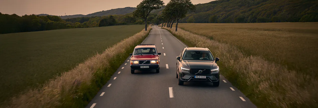 Une vieille Volvo rouge roule sur la voie de gauche, une Volvo neuve grise roule également sur la voie de droite.
