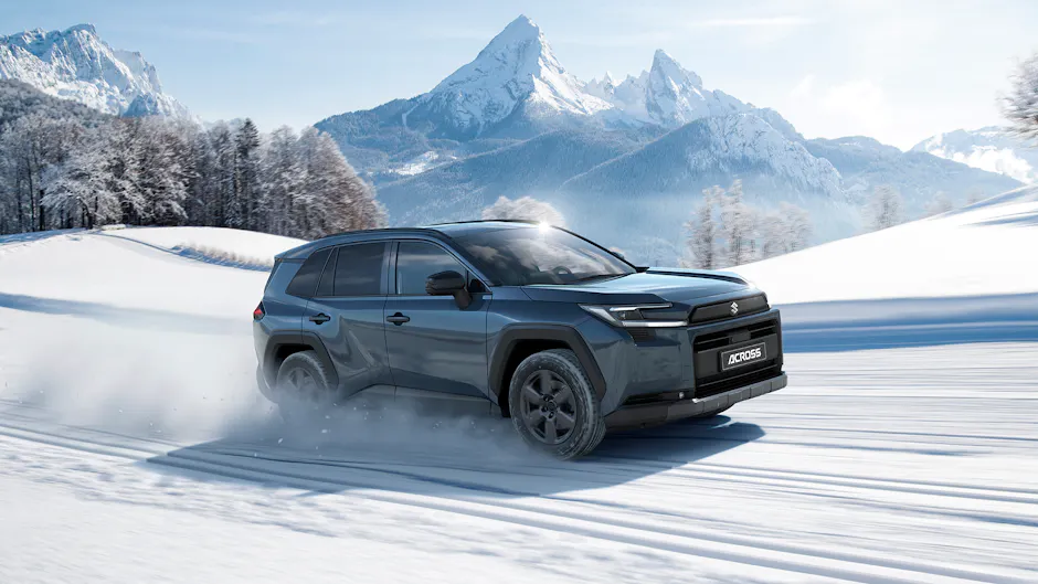 Suzuki Across in Schwarz, fährt im Schnee, im Hintergrund eine verschneite Berglandschaft