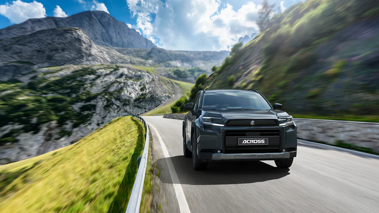 Suzuki Across in Schwarz, fahrt auf einer Passstrasse, im Hintergrund ist ein Berg