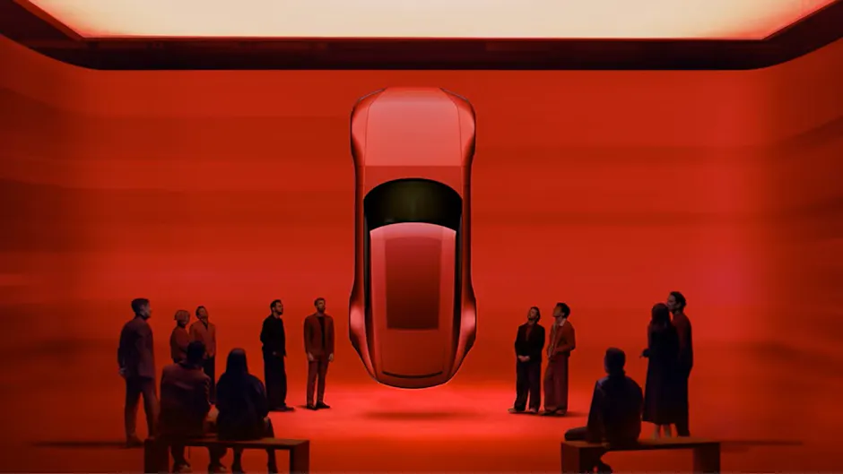 Jaguar Type 00 in rosso, sospesa in una stanza, mentre alcune persone ammirano l’auto.