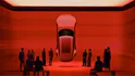 Jaguar Type 00 in rosso, sospesa in una stanza, mentre alcune persone ammirano l’auto.