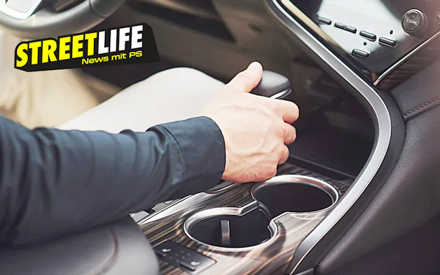 La mano di una persona aziona la leva del cambio nella console centrale di un'auto moderna, accanto al portabevande