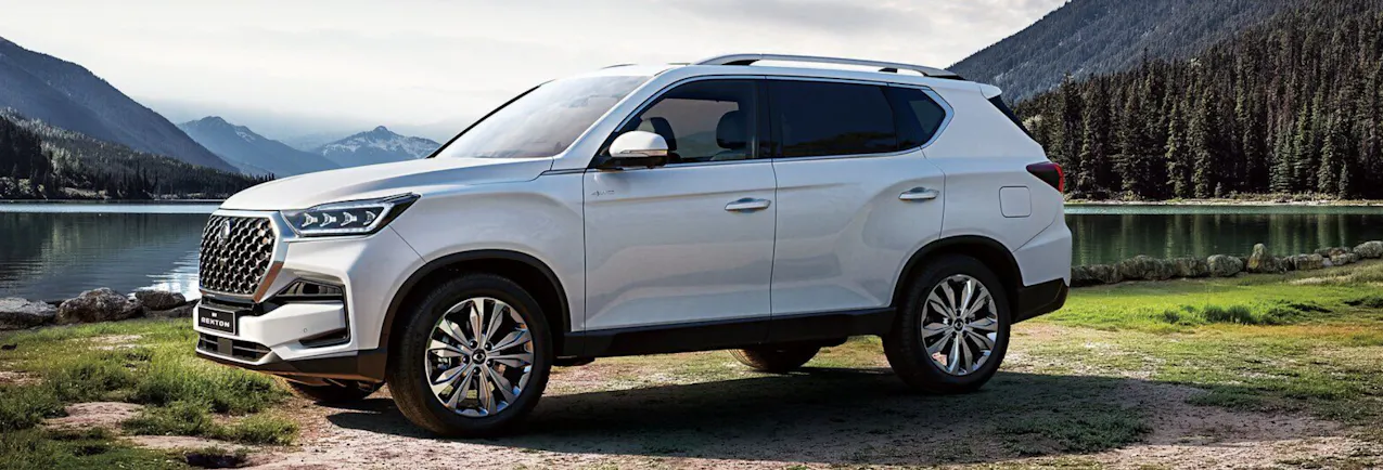 Un KGM Rexton blanc, avec une forêt et un lac en arrière-plan