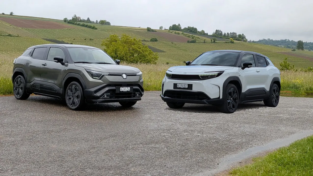 Link ein Suzuki E-Vitara und rechts ein weisser Toyota Urban Cruiser, im HIntergrund sind grüne Wiesen