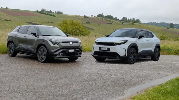 Link ein Suzuki E-Vitara und rechts ein weisser Toyota Urban Cruiser, im HIntergrund sind grüne Wiesen