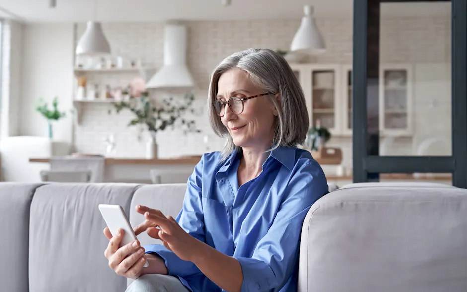 Alte Frau sitz mit Handy auf dem Sofa
