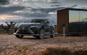 Lexus RZ in Grau während dem Laden in der Wüste, modernes Glashaus nebenan