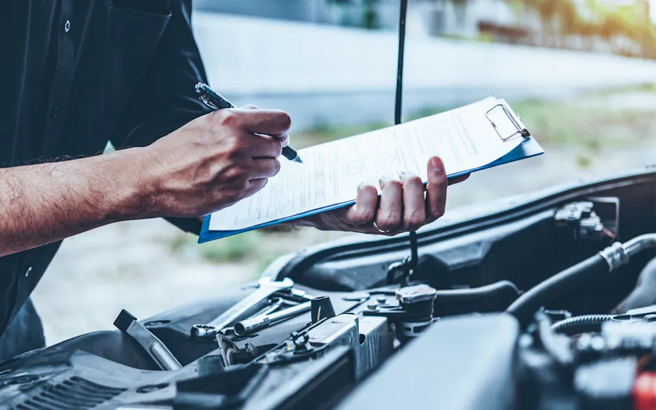 Mechaniker mit Checkliste in der Hand bei geöffneter Motorhaube